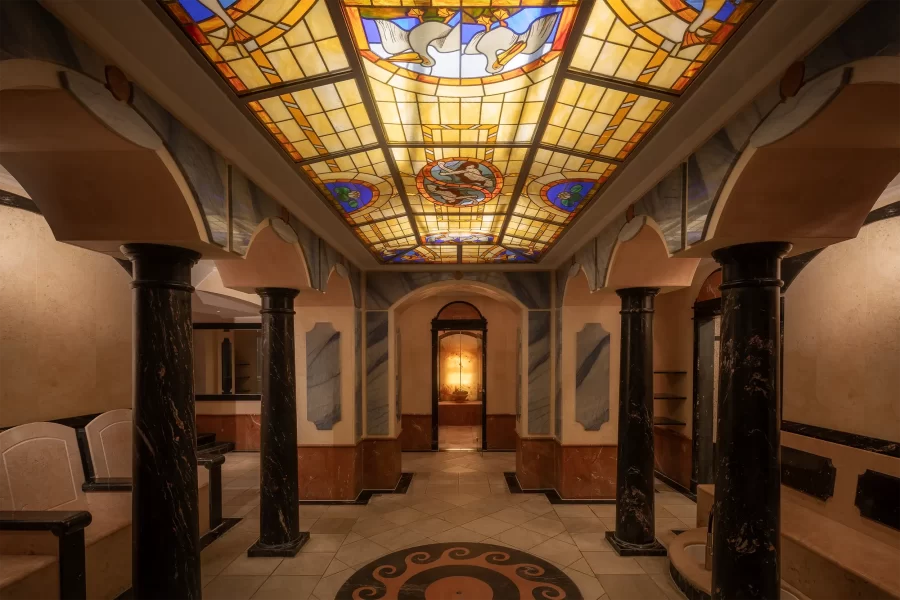 Eingangsbereich des historischen Spa-Bereichs im Hotel Fürstenhof in Bad Bertrich mit römisch inspirierten Säulen und farbiger Glasdecke.