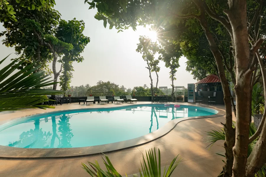Tropischer Poolbereich eines Resorts mit geschwungener Poolform, Lounge Chairs und umgebender Vegetation im warmen Abendlicht.
