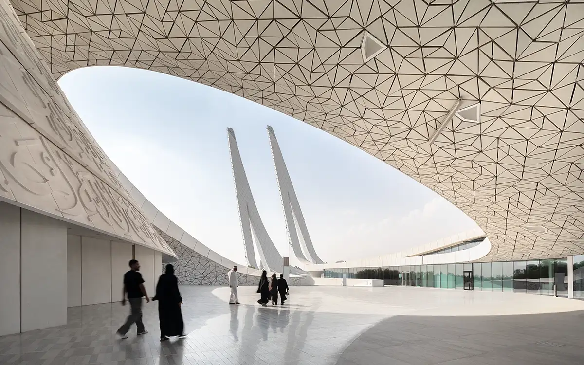 Fotografie architektury HBKU Minaretein v Dauhá zachycující moderní islámský design – Pohled na dva šikmé minarety tyčící se k nebi, rámované geometrickou střešní konstrukcí a kaligraficky zdobenými stěnami.