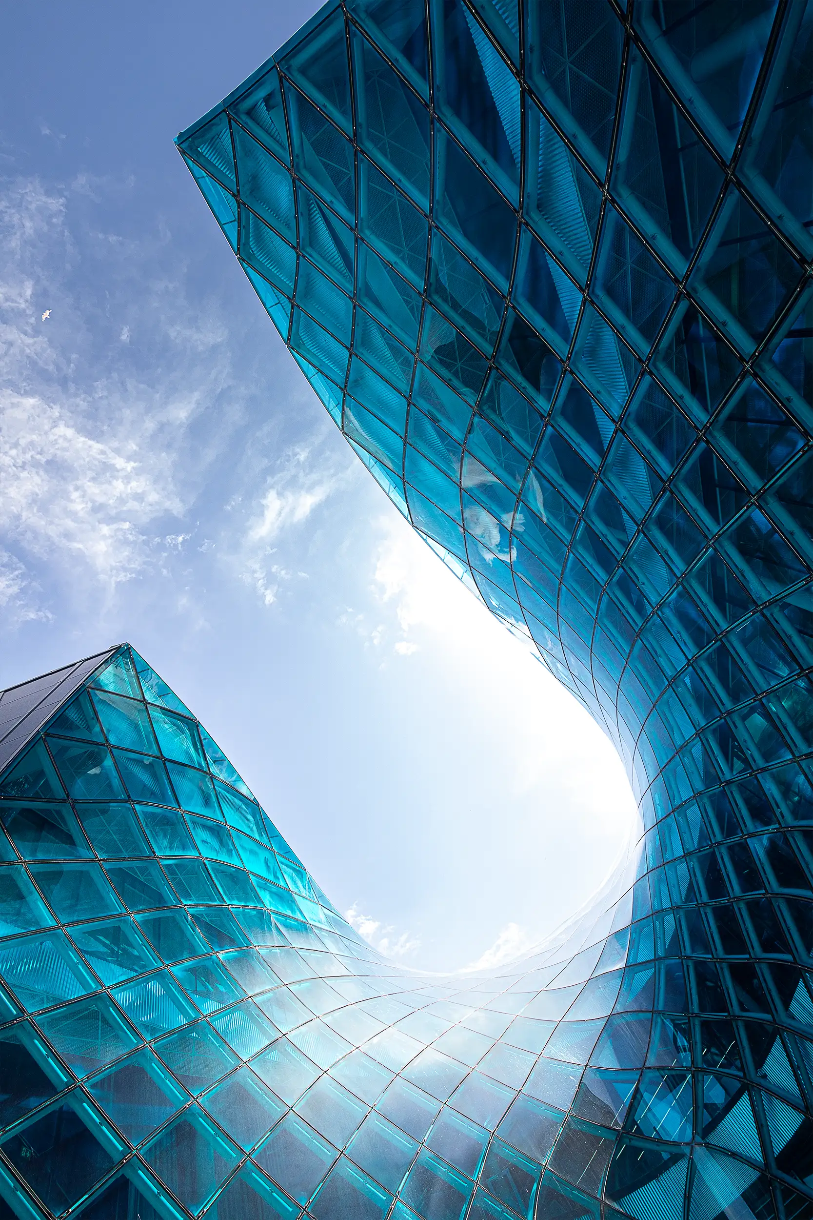 Detail moderní, fluidní architektury nákupního centra Emporia v Malmö s zaměřením na vlnový výkus do modrého skleněného opláštění budovy.