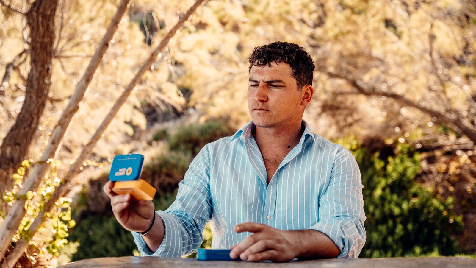 Nick looks thoughtfully at an open tin of mastic gum while sitting in nature.