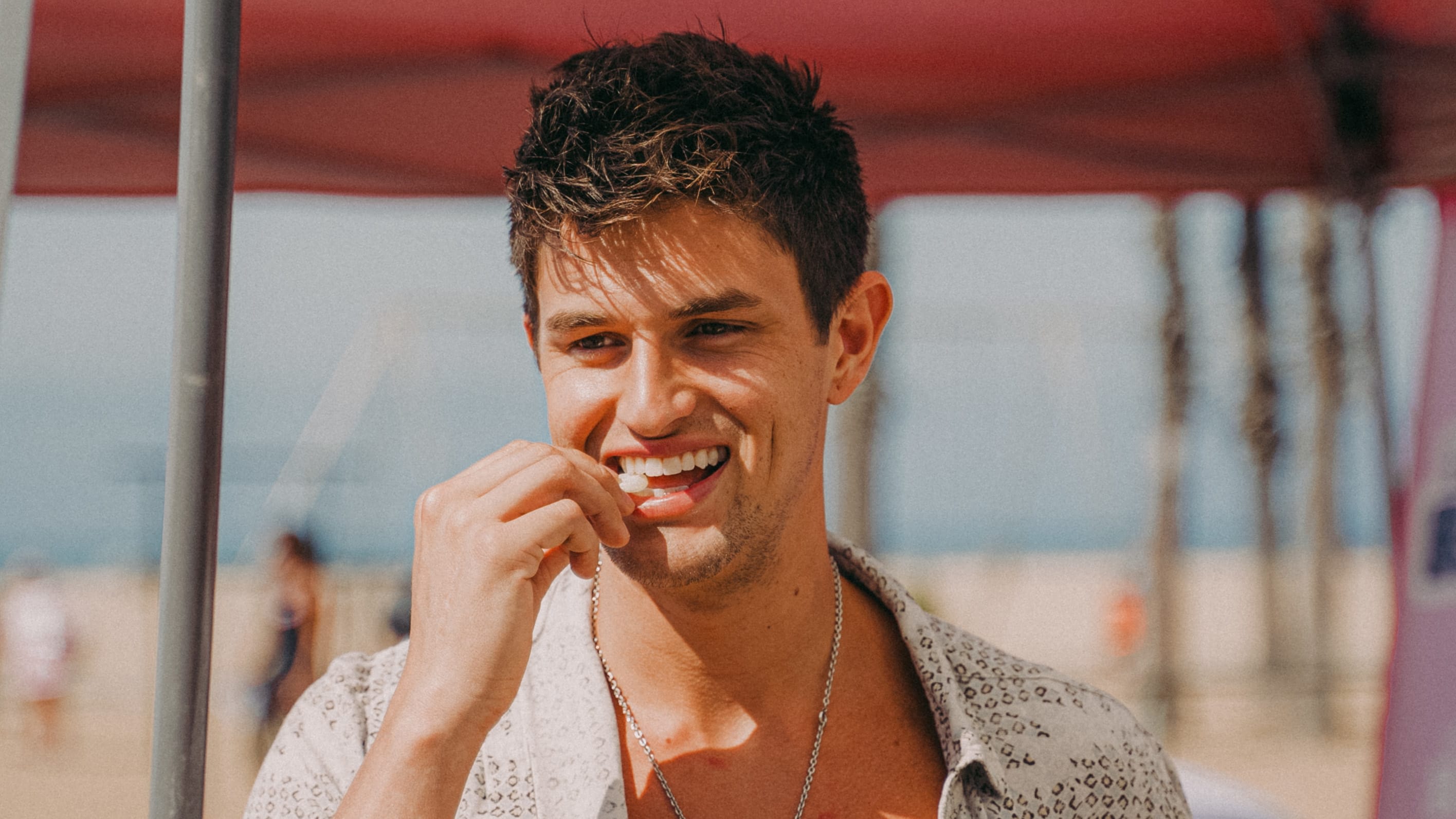 A man with brown hair and a white shirt puts a piece of mastic gum in his mouth
