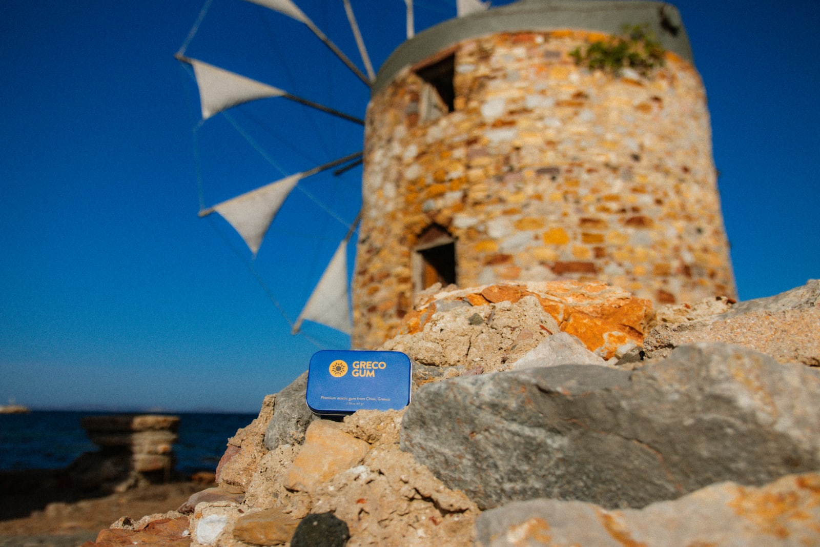 Greco Gum tin on a rocky shore, in front of a beachside windmill in Chios, Greece