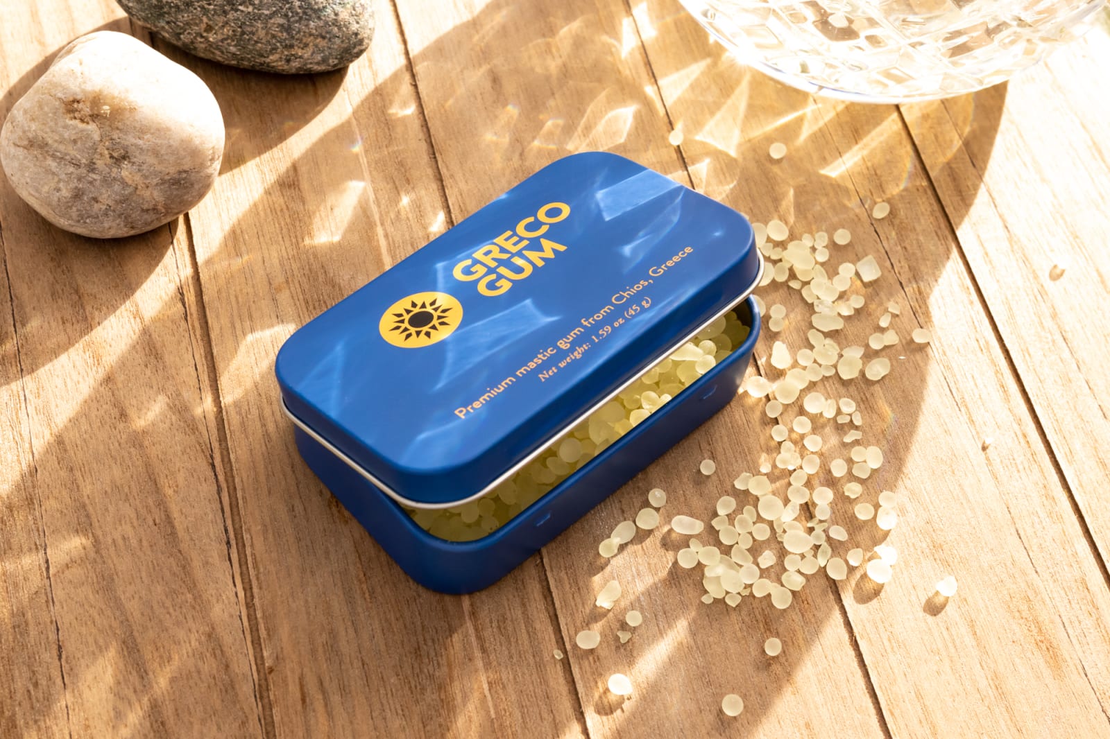 Sunlight casting a shadow through a crystal glass over a blue tin of Greco Gum
