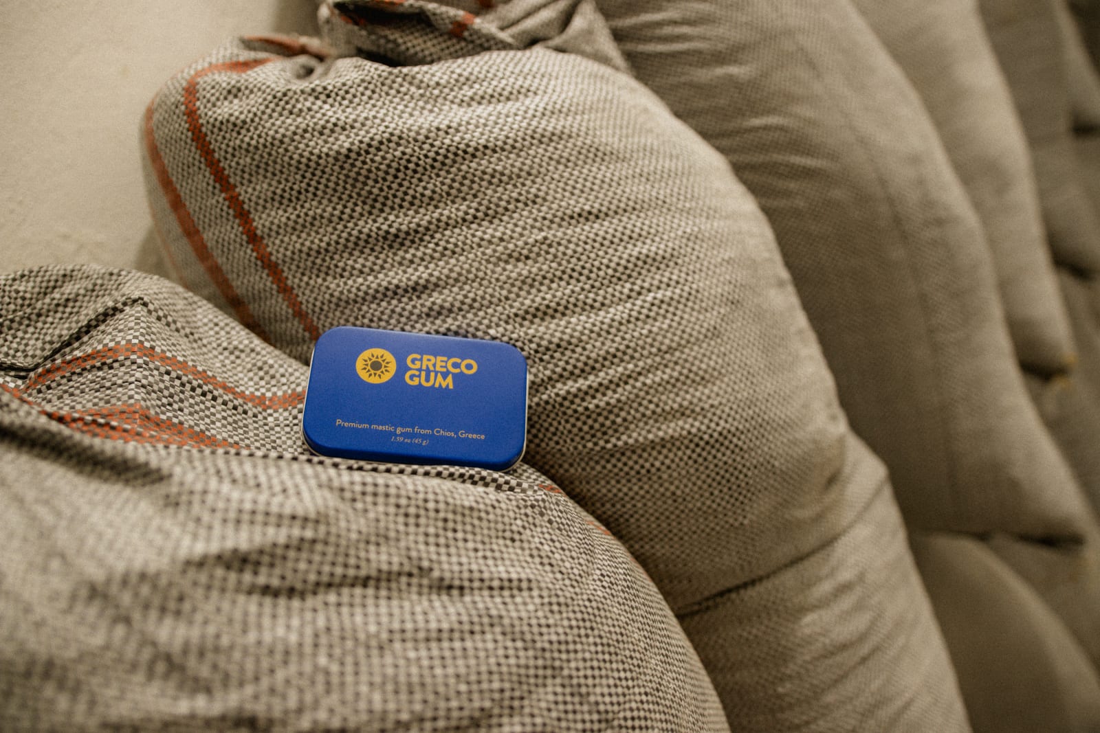 A blue tin of Greco Gum sits on top of a pile of large canvas sacks