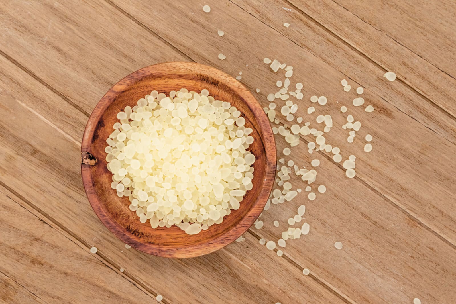 Top-down view of a wooden bowl filled with Greco Gum mastic droplets.