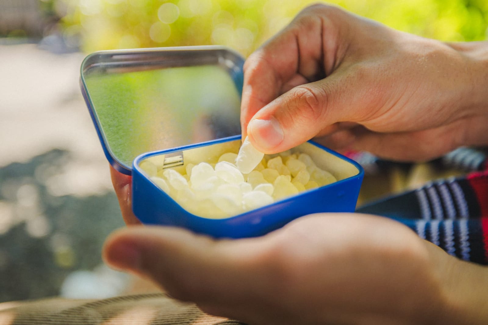 A zoomed-in shot of a hand reaching into an open tin of Greco Gum.