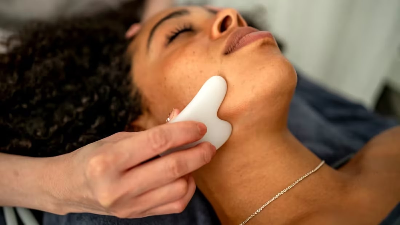 A woman receives a gua sha face massage with a stone tool