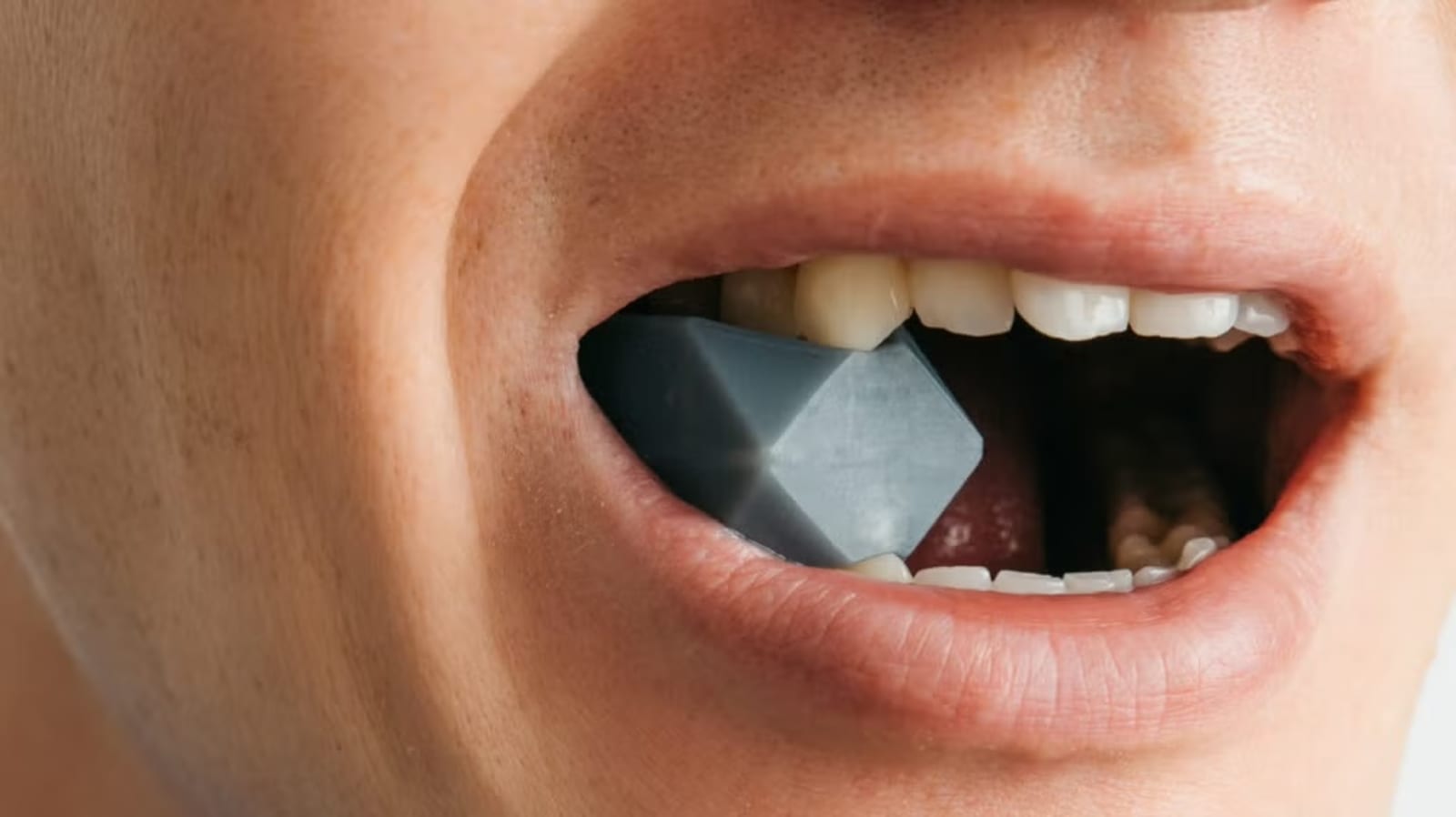 A man chews a chunk of hard plastic to attempt to grow his jaw muscles