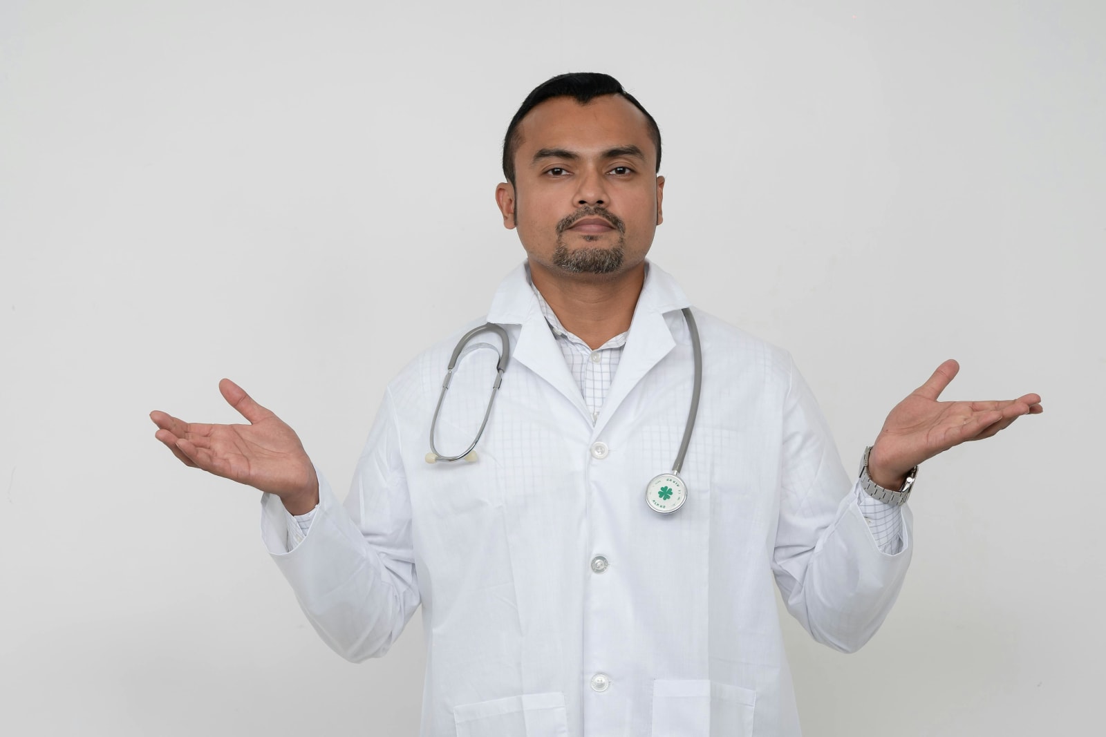 A doctor in a white coat and stethoscope around his neck shrugs