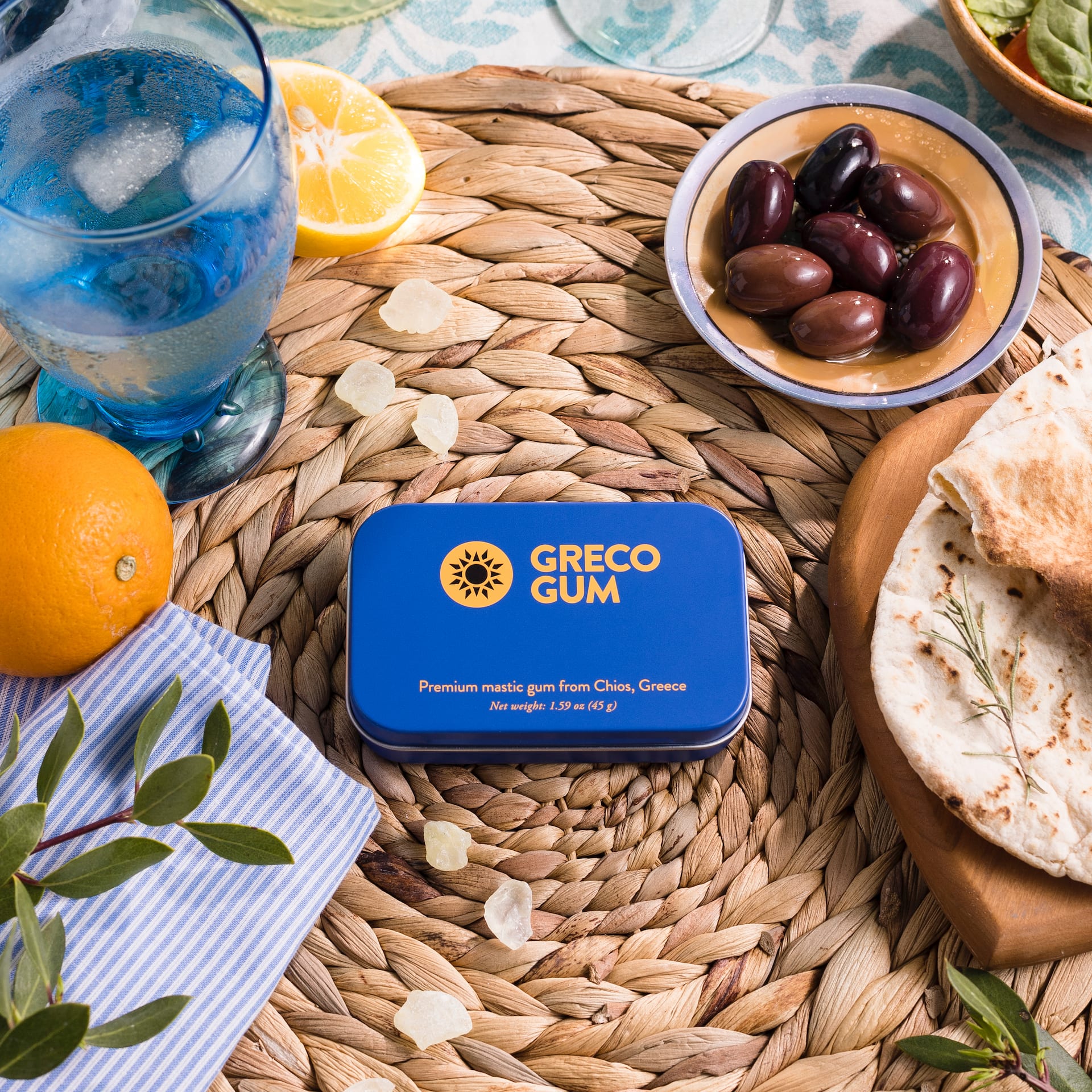 Mastic gum centered in a table setting with water, fruits, and herbs