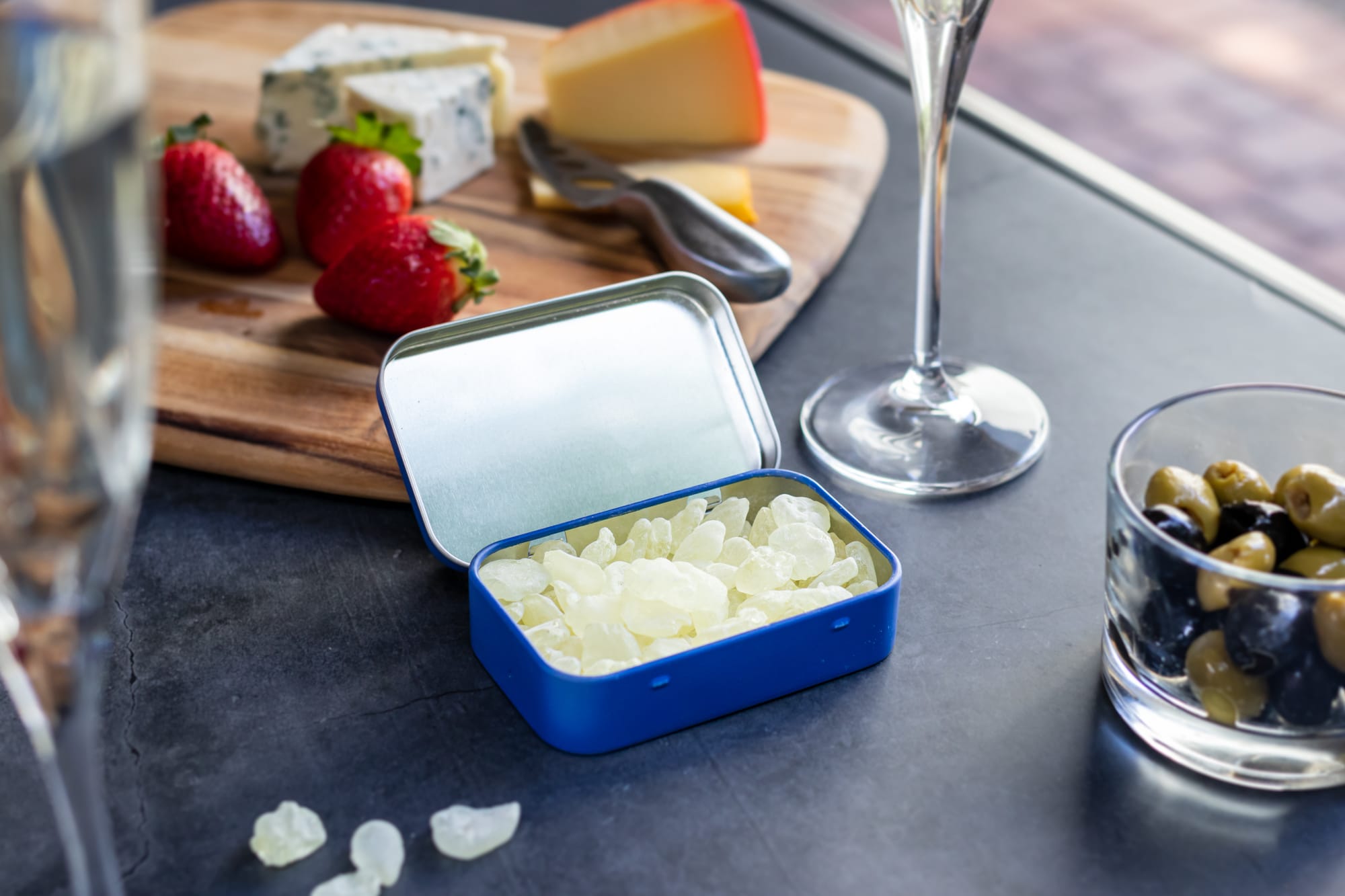 Tin of mastic nuggets next to fruit and cheese.