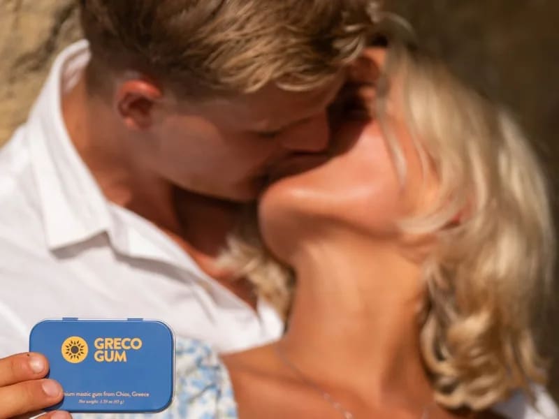 A couple sharing a kiss, one holding a Greco Gum tin