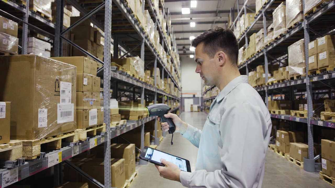 Hình ảnh nhân viên đang quét mã vạch/RFID trên kiện hàng trong kho bãi hiện đại, máy tính bảng hiển thị thông tin