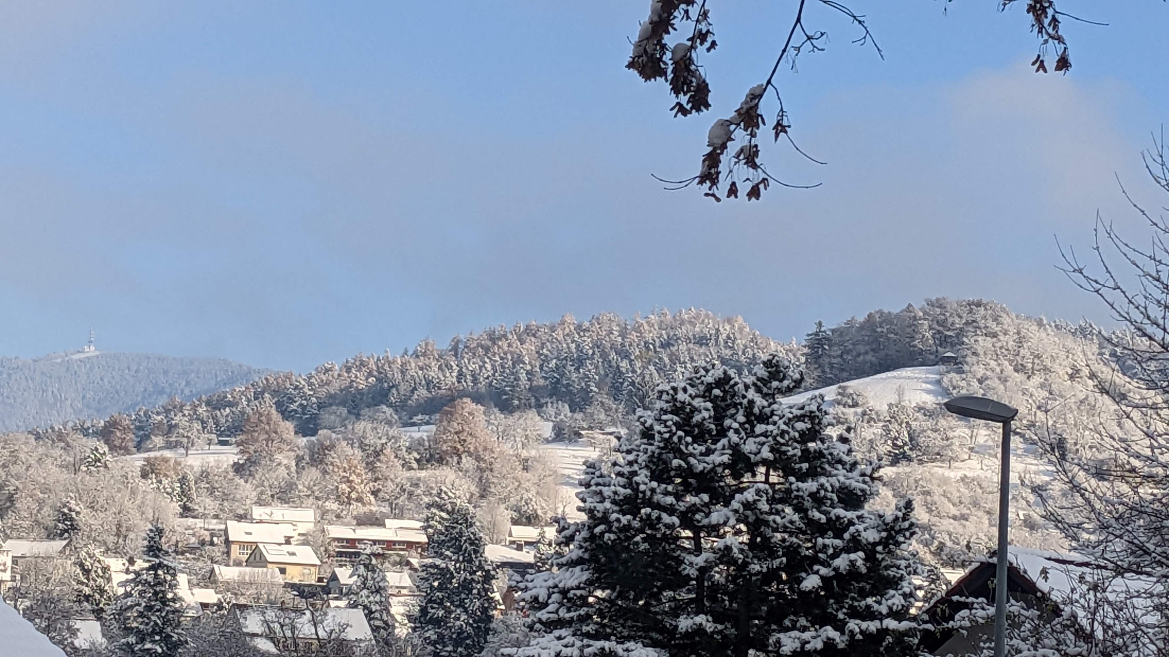 Close-up of a person riding a skateboard, focusing on their feet and the board. One foot is on the board, while the other foot is up, in motion. A skatepark is blurred in the background.