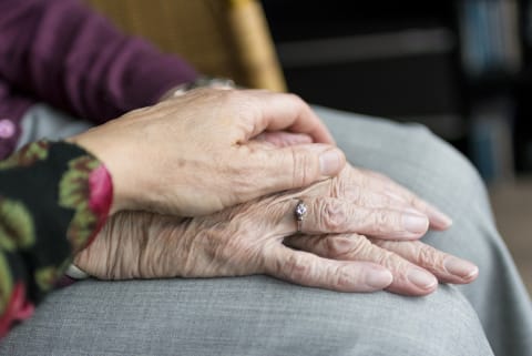 Eine junge Hand liegt tröstend auf einer älteren Hand.