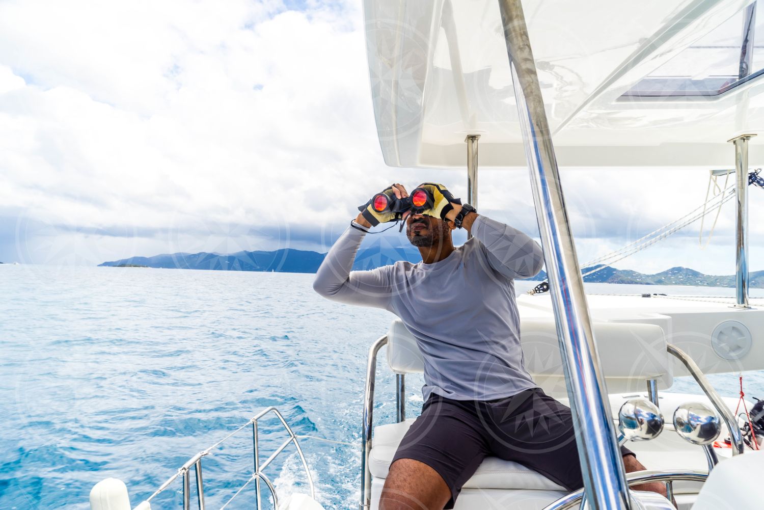 Man at helm of sailboat looking through binoculars