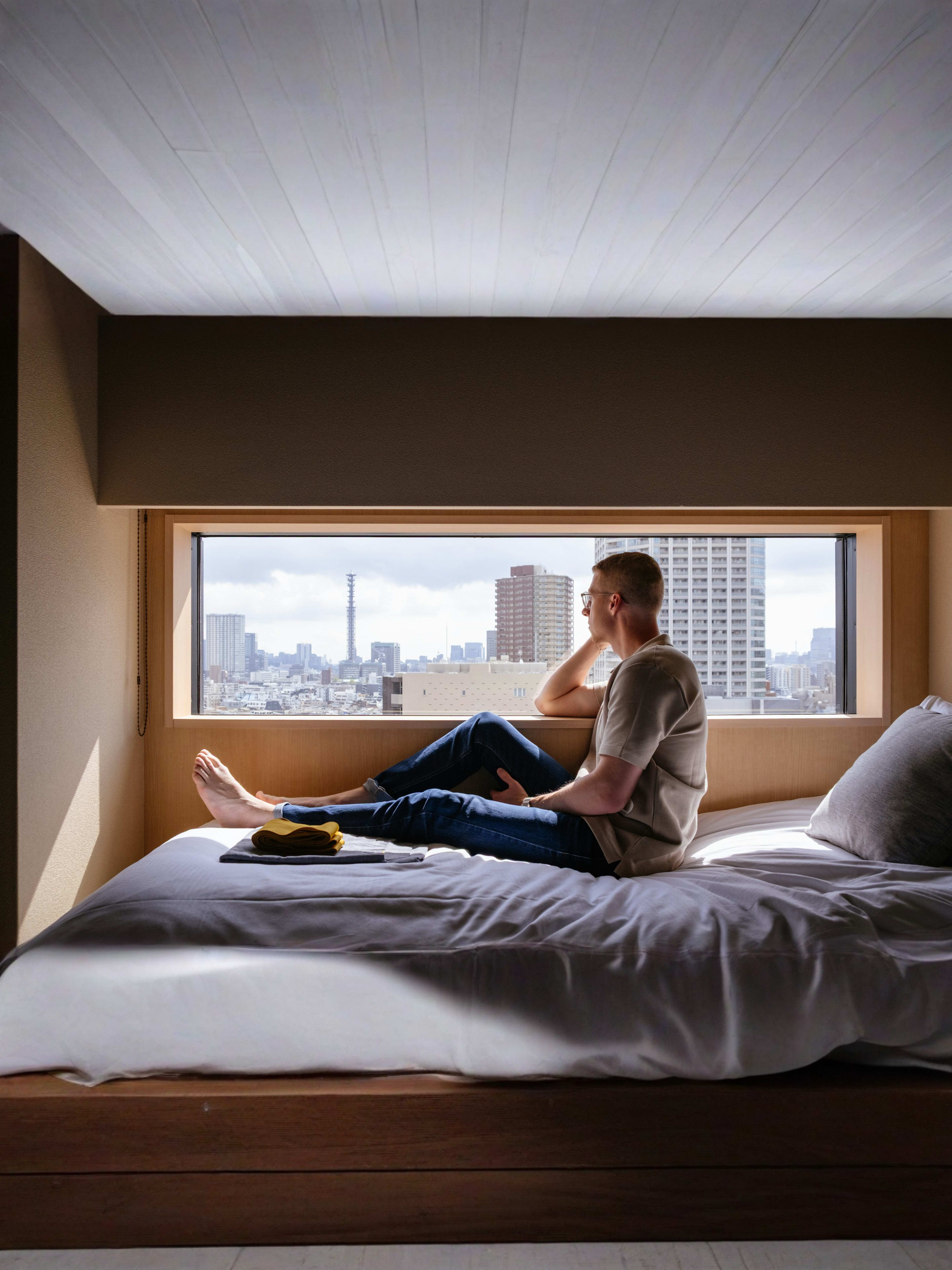  Man relaxes on a bed, gazing at a city view.