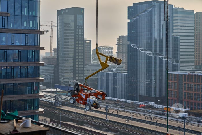 een hoogwerker wordt via bouwkraan verplaatst