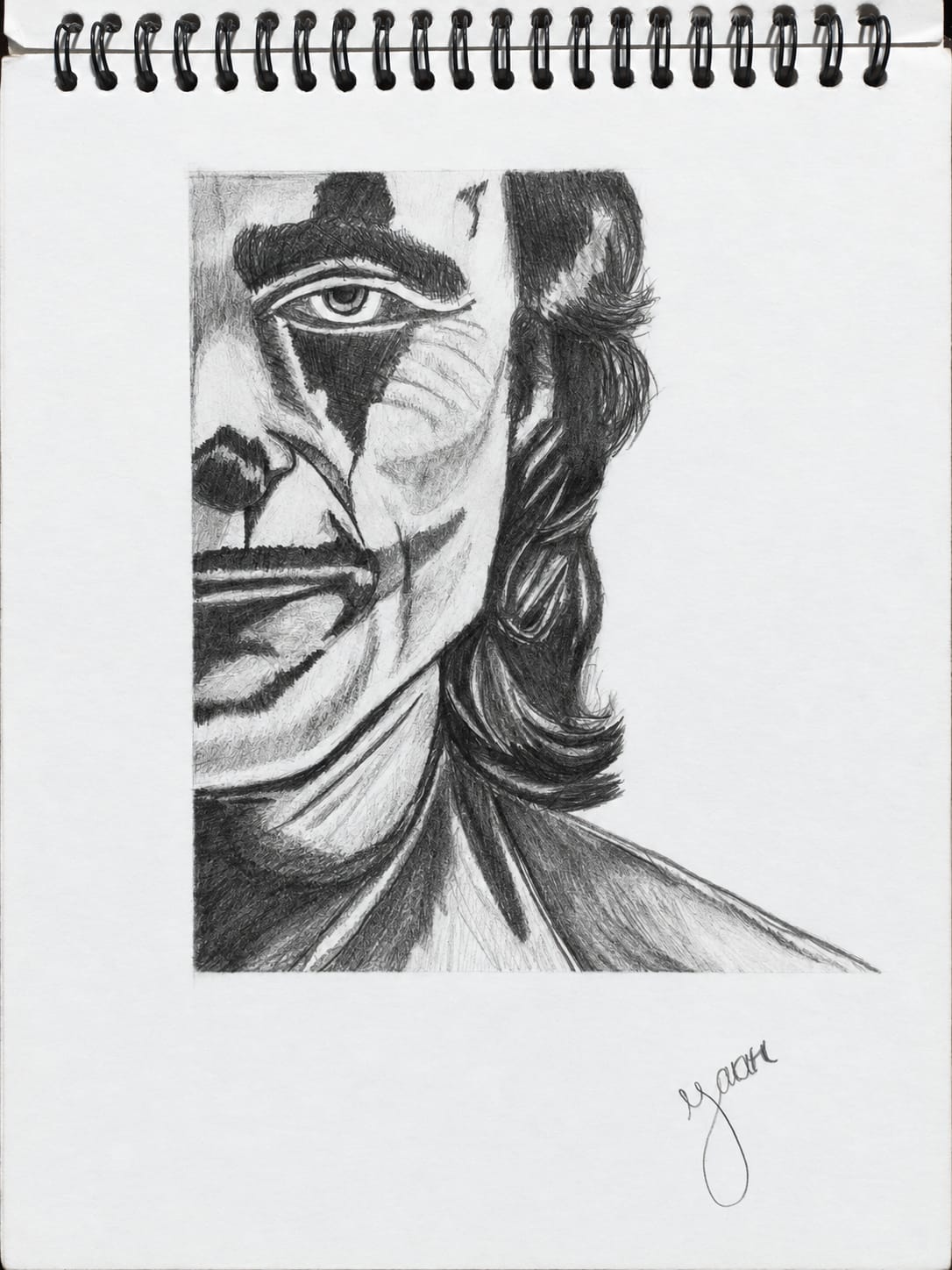 A graphite pencil portrait of the Joker showing a close-up view of half his face, with a sharp intense eye, dark shadowed features, messy hair, and a dramatic contrast between light and darkness on a sketchbook page.