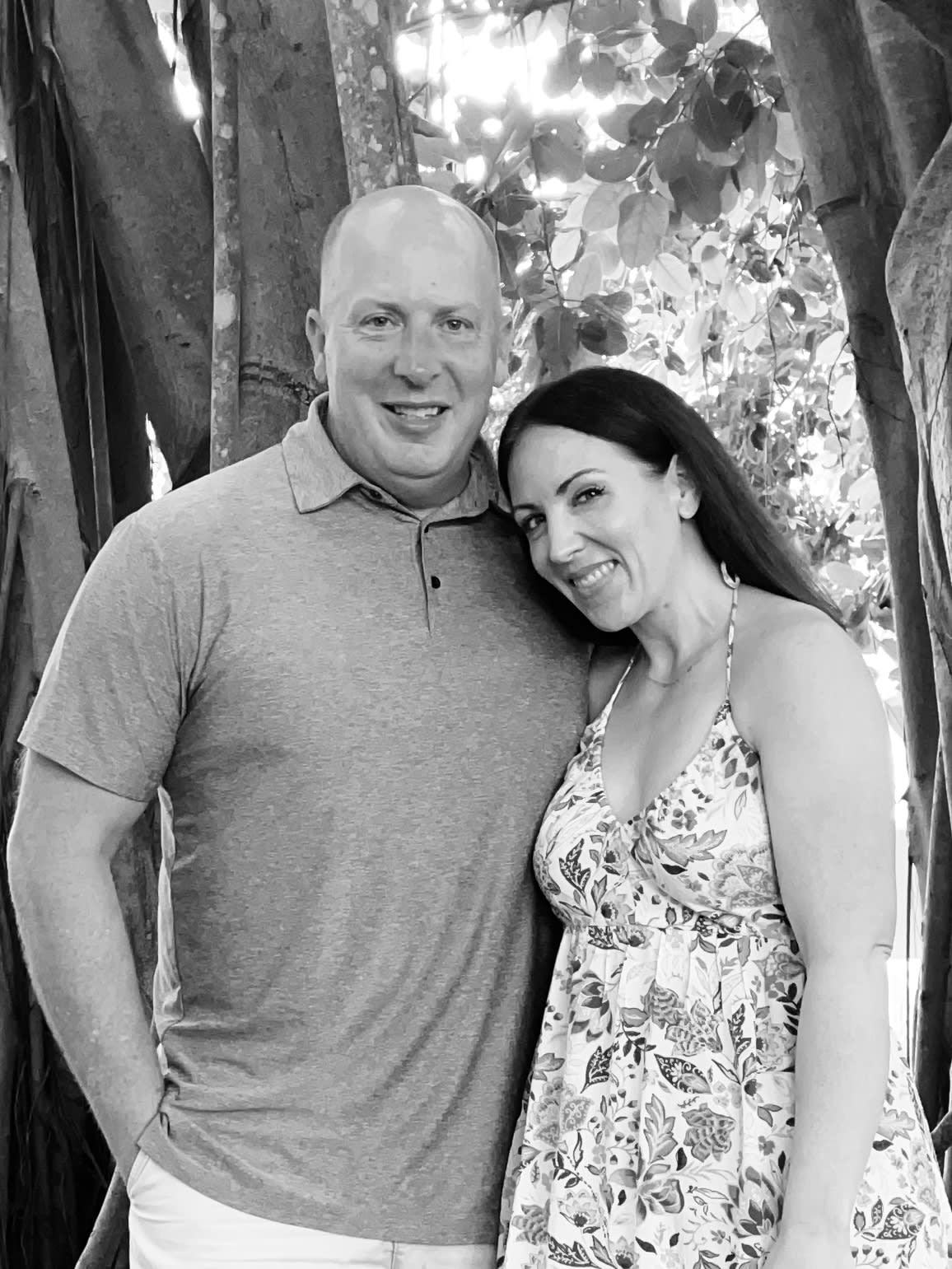 Brian and his wife smiling outdoors beneath a large banyan tree