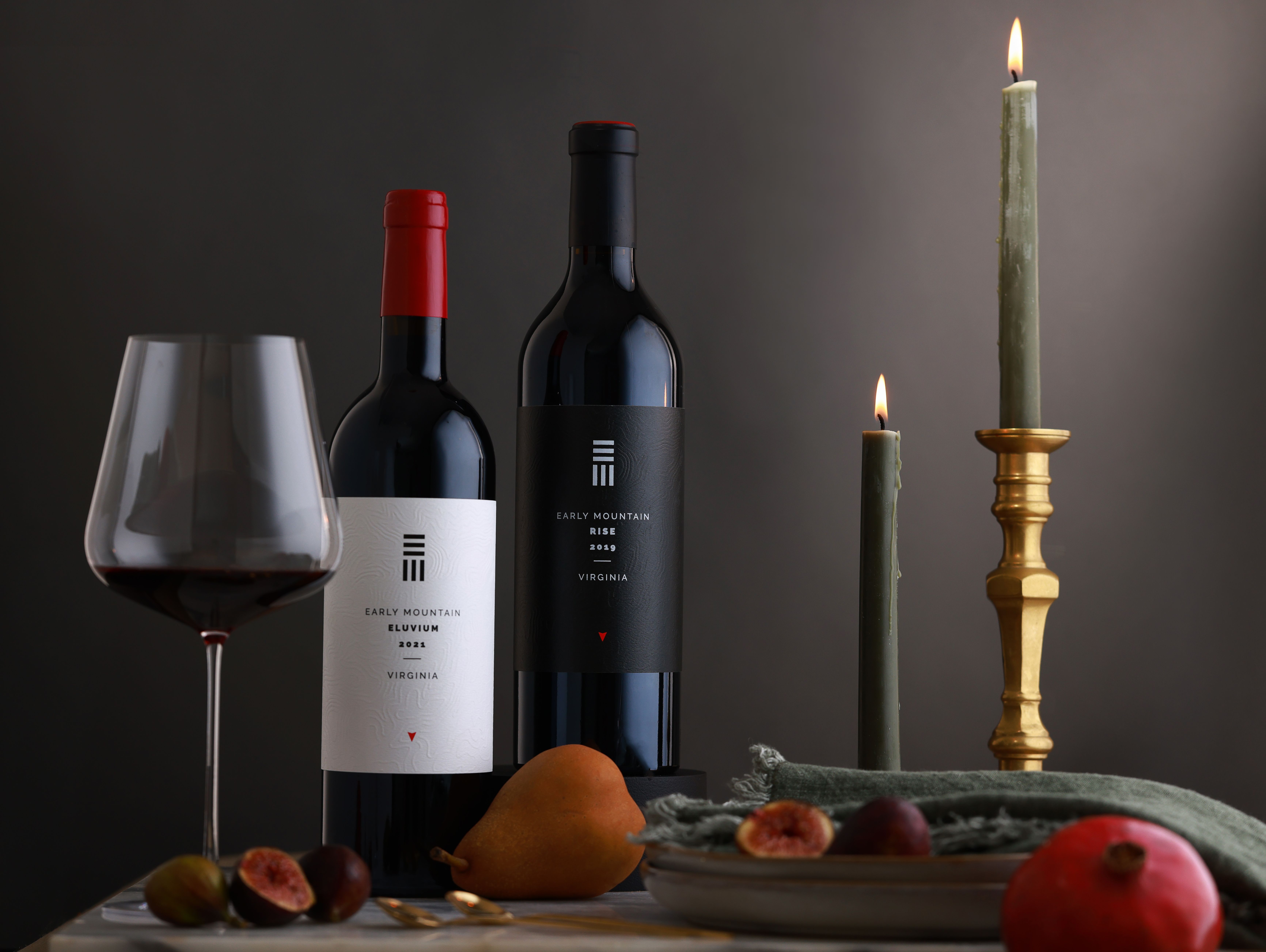 A bottle of red wine, a bottle of white wine, and a candle on a table.