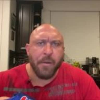 Bald Guy Eating Chips meme template: A bald, heavily bearded man in a red t-shirt is looking at the camera with a perplexed expression, holding a small blue object in his left hand, and has just taken a bite out of a chip.