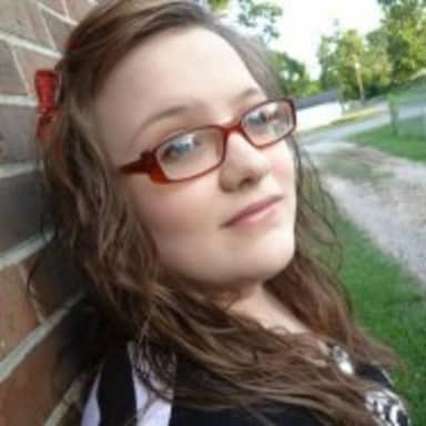 Bad Luck Hannah meme template: A young woman with glasses and a red bow in her hair, looking directly at the camera with a slight, knowing smile.