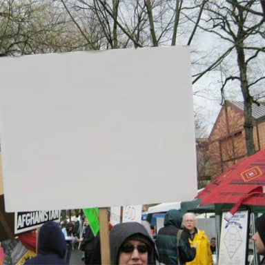Blank Protest Sign meme template: A blank white protest sign is held up in front of a crowd. Other signs and tents are visible in the background.