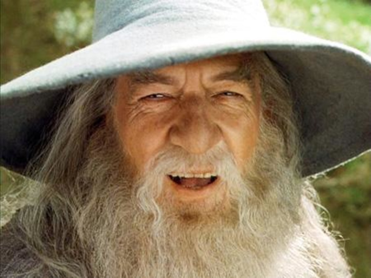 A Wizard Is Never Late meme template: Close-up of Gandalf the Grey's face from The Lord of the Rings, featuring his iconic hat, beard, and a knowing, slightly mischievous expression.
