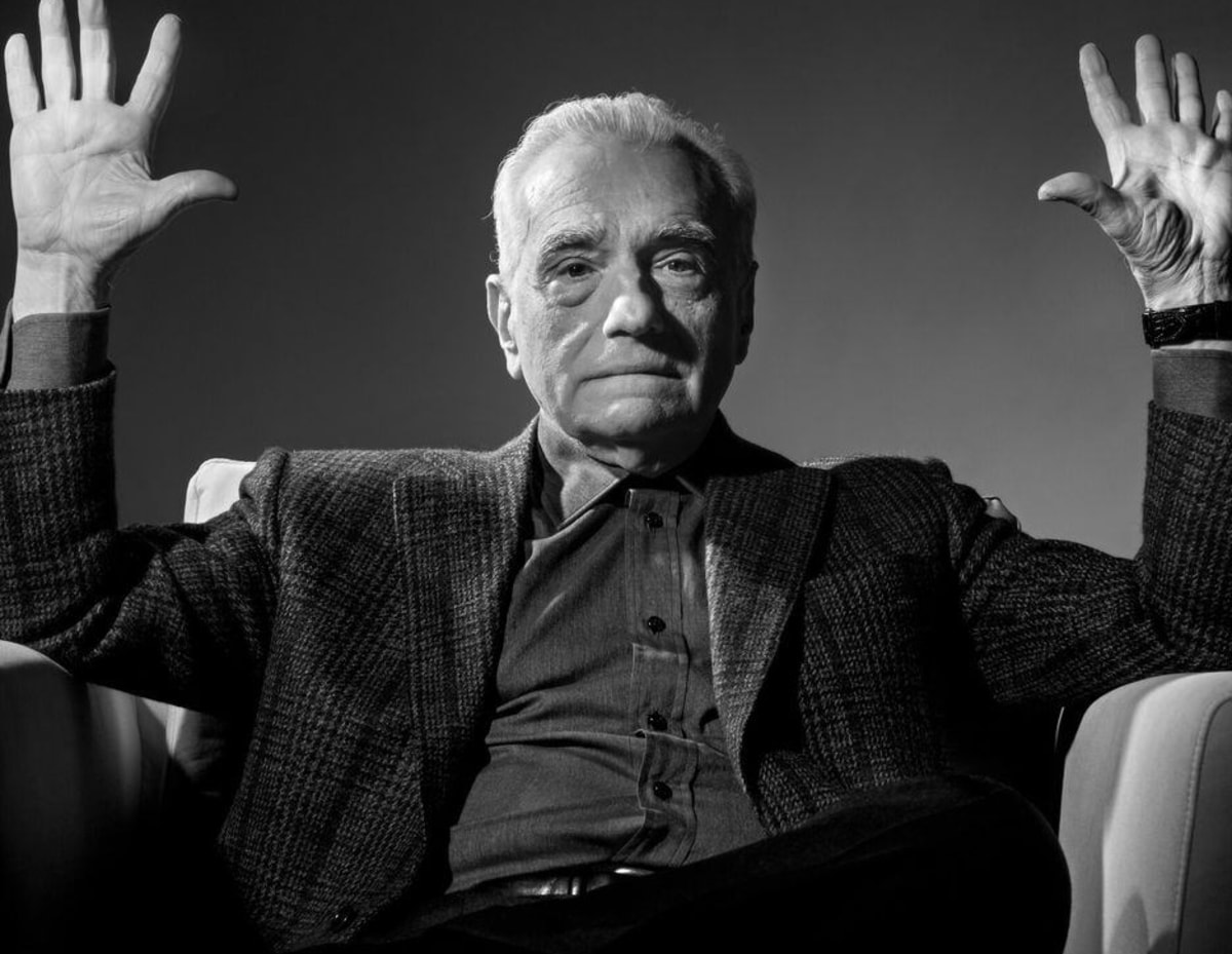 Absolute Cinema meme template: A man sits in a chair with his arms raised and palms facing forward, in a pose of either defense, surrender, or explanation.