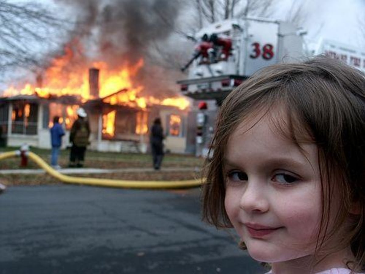 Disaster Girl meme template: A young girl smirks at the camera in the foreground, while a house burns in the background with firefighters and a fire truck present.