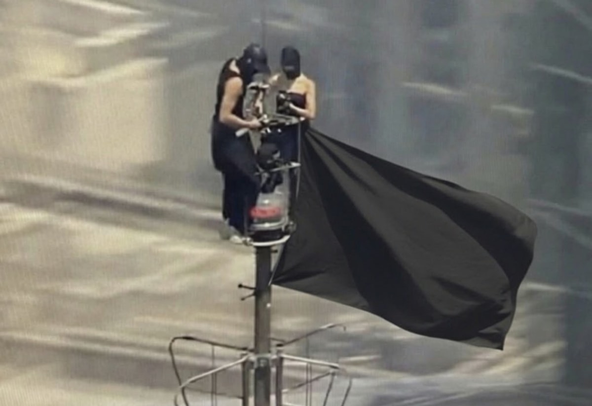 Empire State Building Climbers meme template: Two figures on a high platform at the top of a pole, one appears to be holding a camera, and a large black flag is unfurling dramatically.