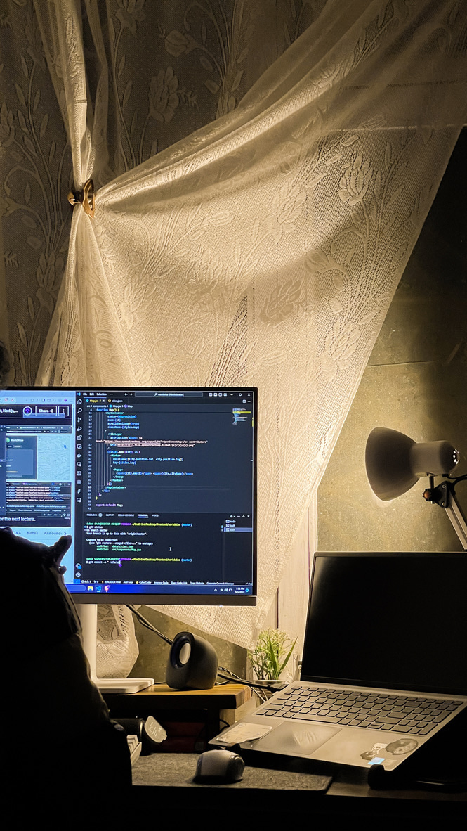 Monitor showing Vue code by lamplight, lit curtain behind