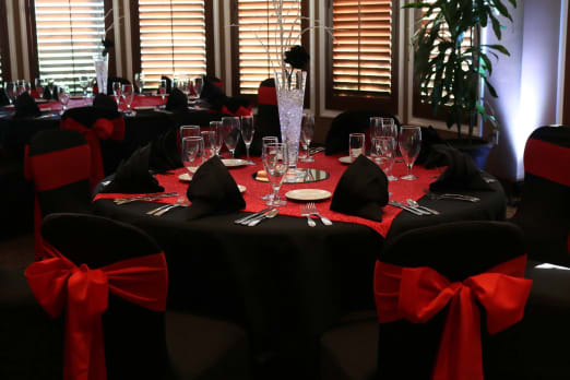 Tables decorated in black & red plus a large flower arrangement in the center, chairs have red bows.