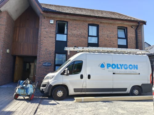 Polygon Property Damage Control van parked outside the brick 'Wellsprings' building, with a pressure washer and cleaning equipment cart beside it