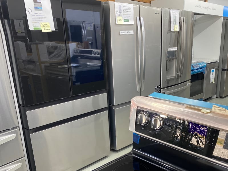 A black-glass Samsung French-door refrigerator beside stainless Whirlpool and GE models at Barn Appliances