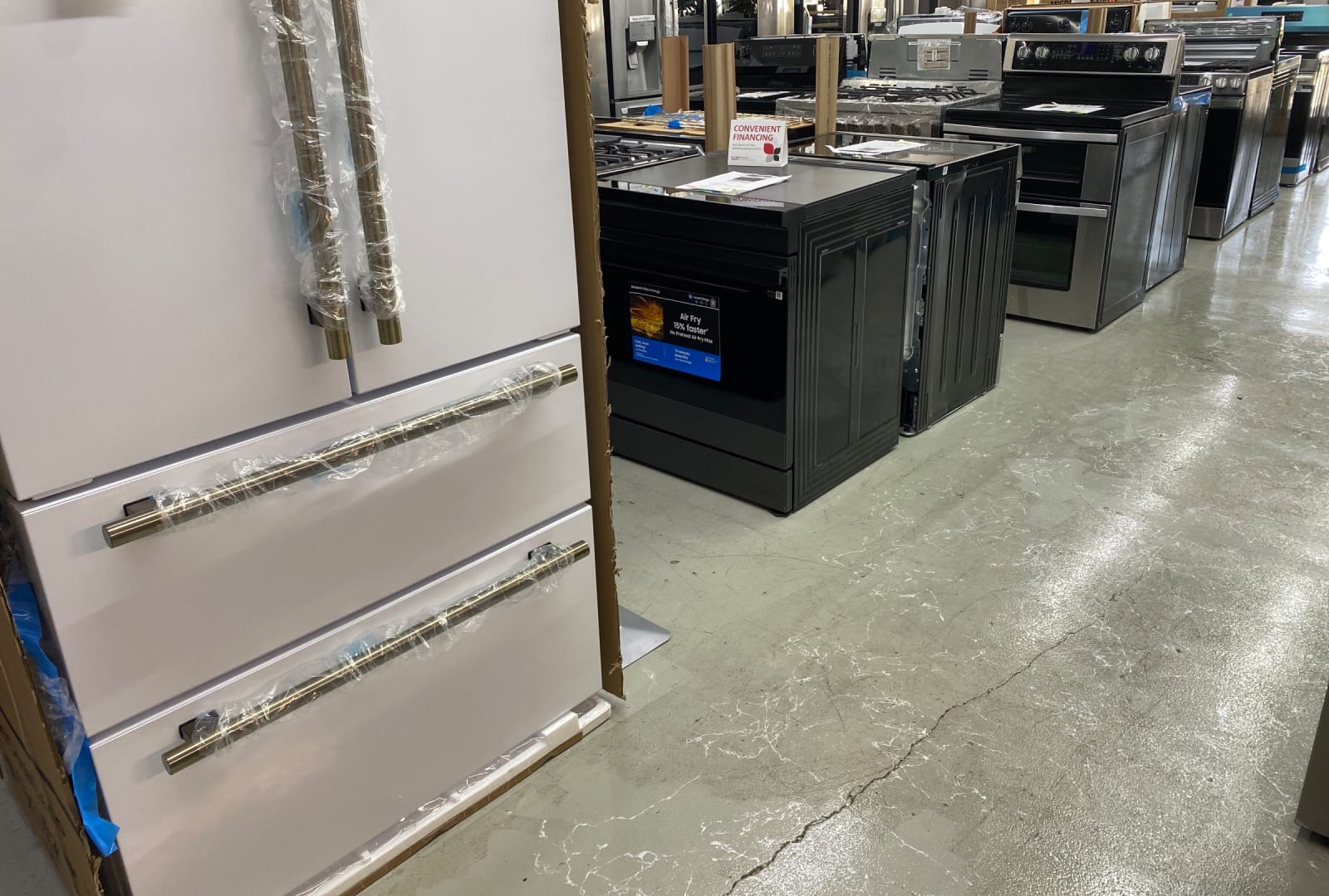 A white French-door refrigerator with brass handles beside black slide-in ranges in the Barn Appliances showroom in Leoma, TN