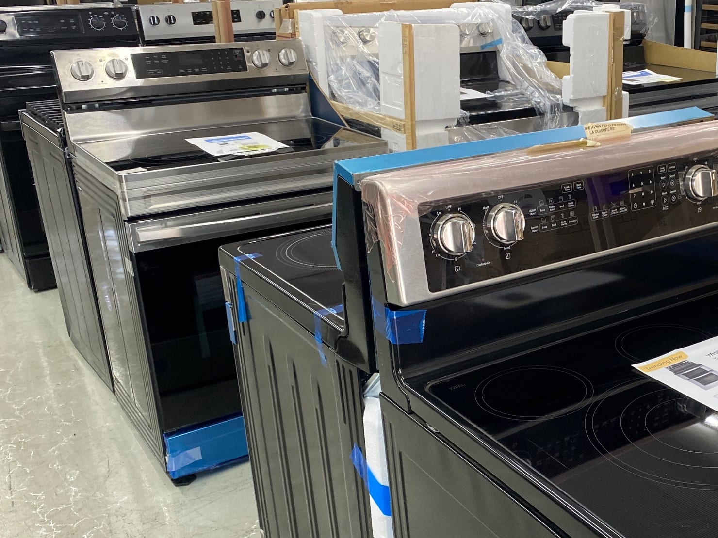 An aisle of new black and stainless ranges, some still wrapped and taped, at Barn Appliances in Leoma, TN