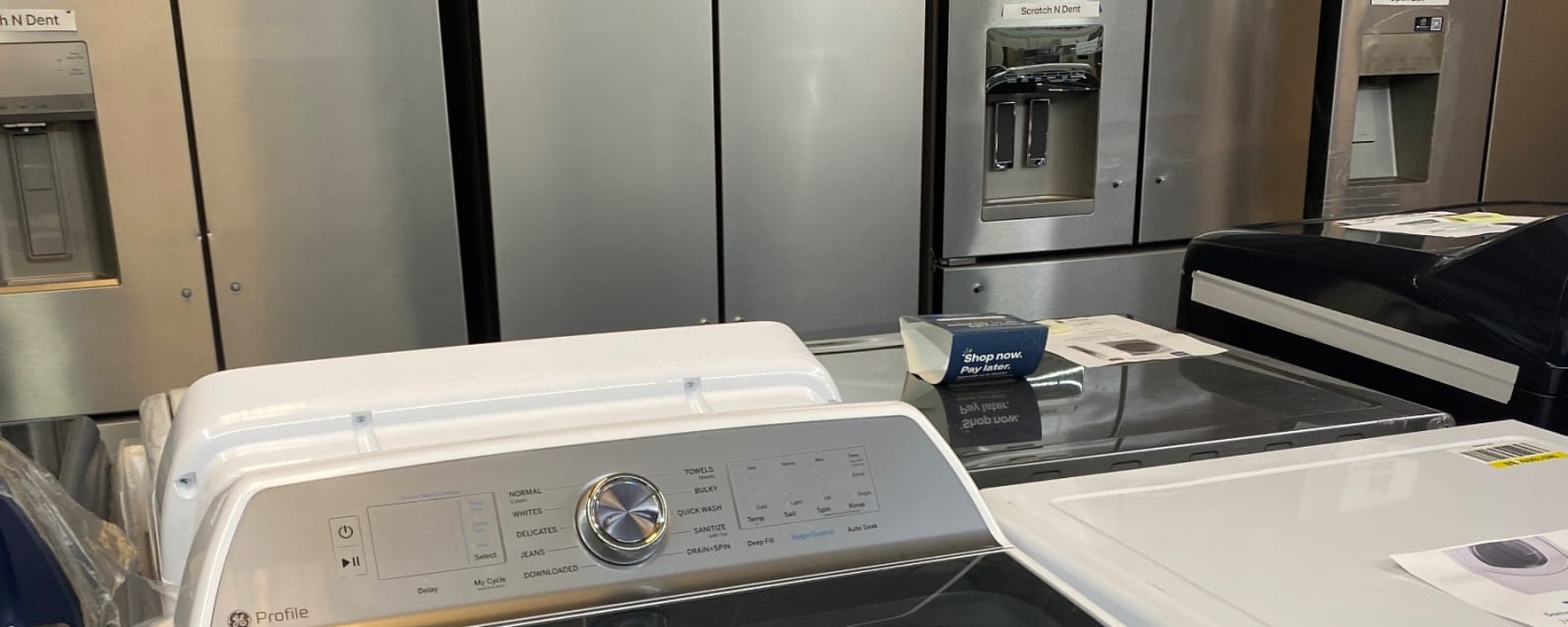 The control panel of a GE Profile top-load washer in front of a row of stainless refrigerators in Leoma, TN