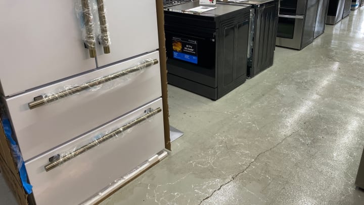 A white refrigerator with brass handles beside black slide-in ranges