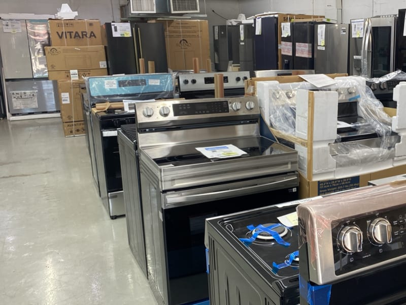 Stainless electric ranges and a black gas range with cast-iron grates lined up down the aisle at Barn Appliances