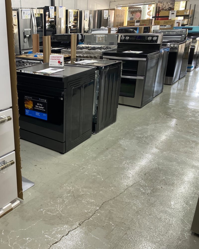 Black slide-in and stainless double-oven ranges lined up down an aisle of the Barn Appliances showroom