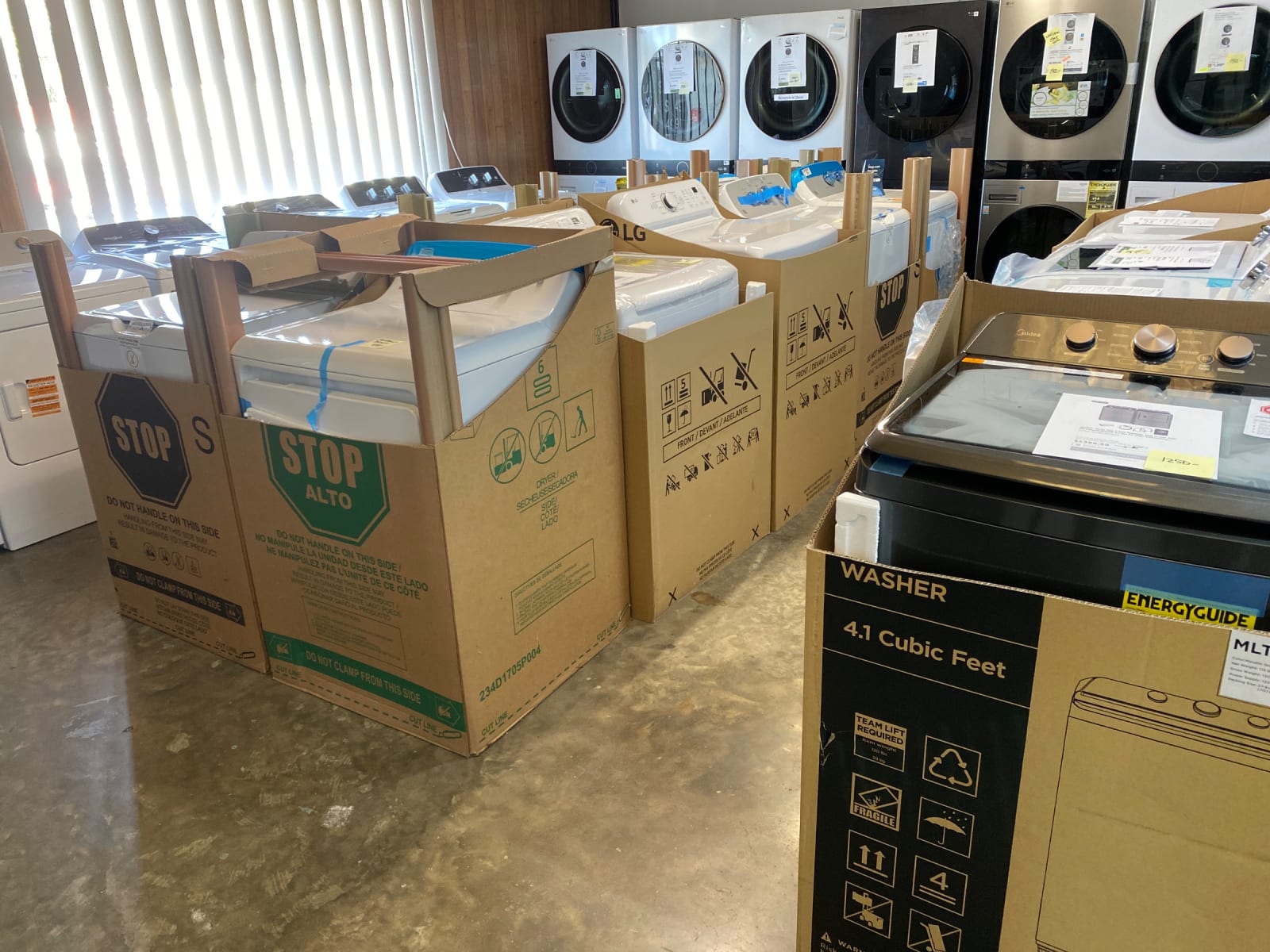 Boxed washers and dryers beside stacked LG laundry centers in the wood-paneled laundry room at Barn Appliances
