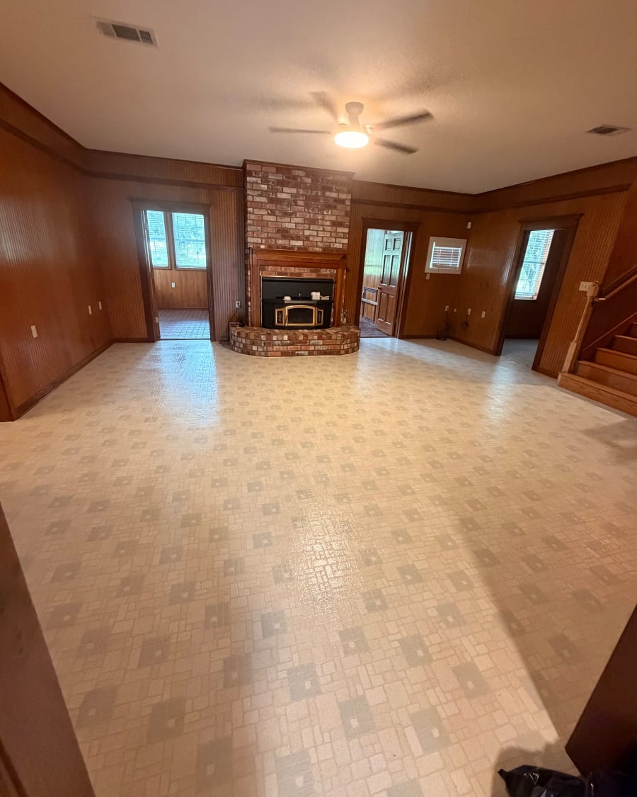 An empty wood-paneled living room with a brick fireplace and a clean, shining floor