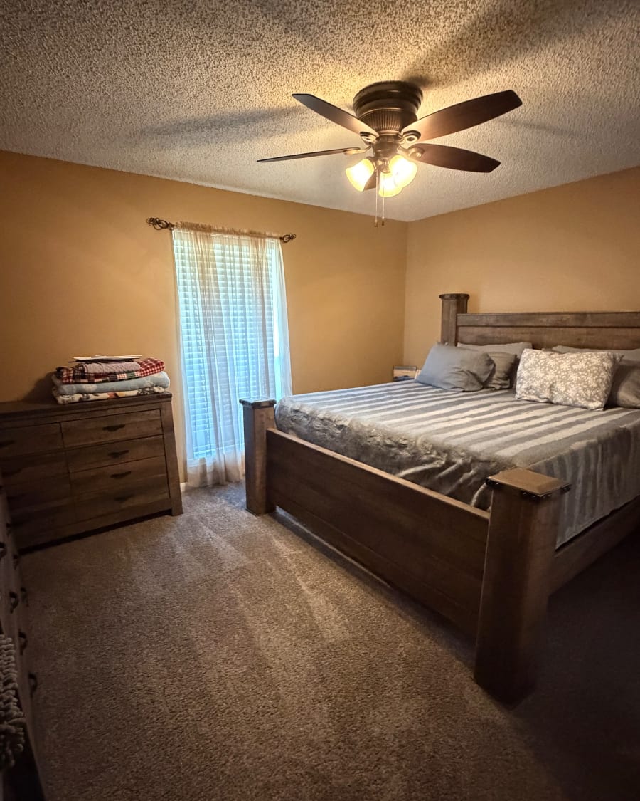 A tidy bedroom with a made bed and fresh vacuum lines in the carpet