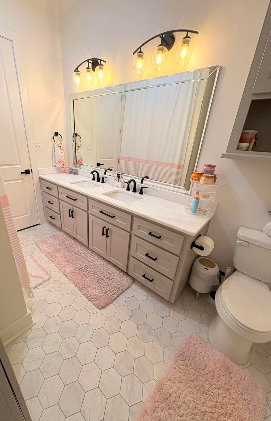 A cleaned bathroom with a double vanity, hexagon tile floor and pink rugs