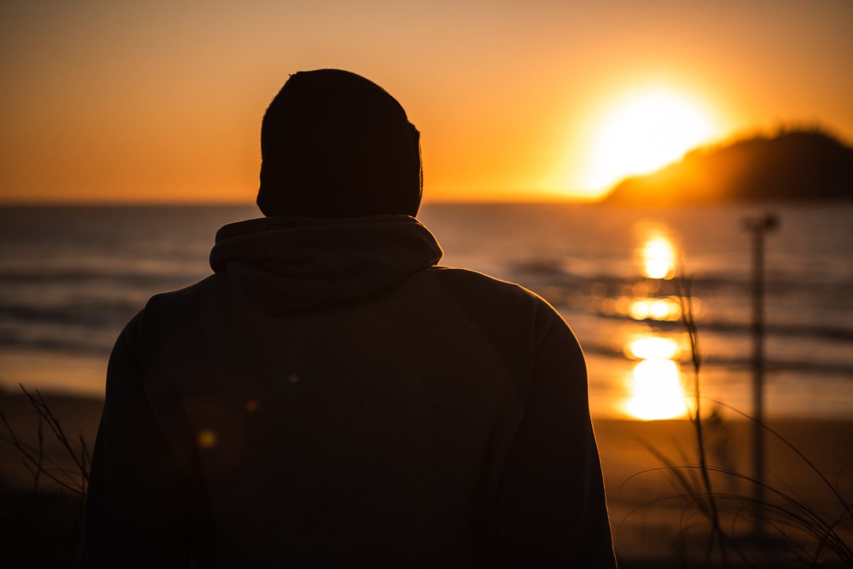 Pessoa de costas olhando o nascer do sol sobre o mar, com uma ilha ao fundo