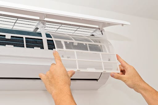 Hands replace an air conditioning filter