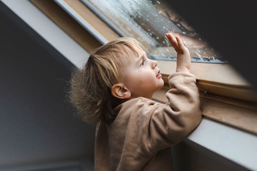 Child looks out rainy window